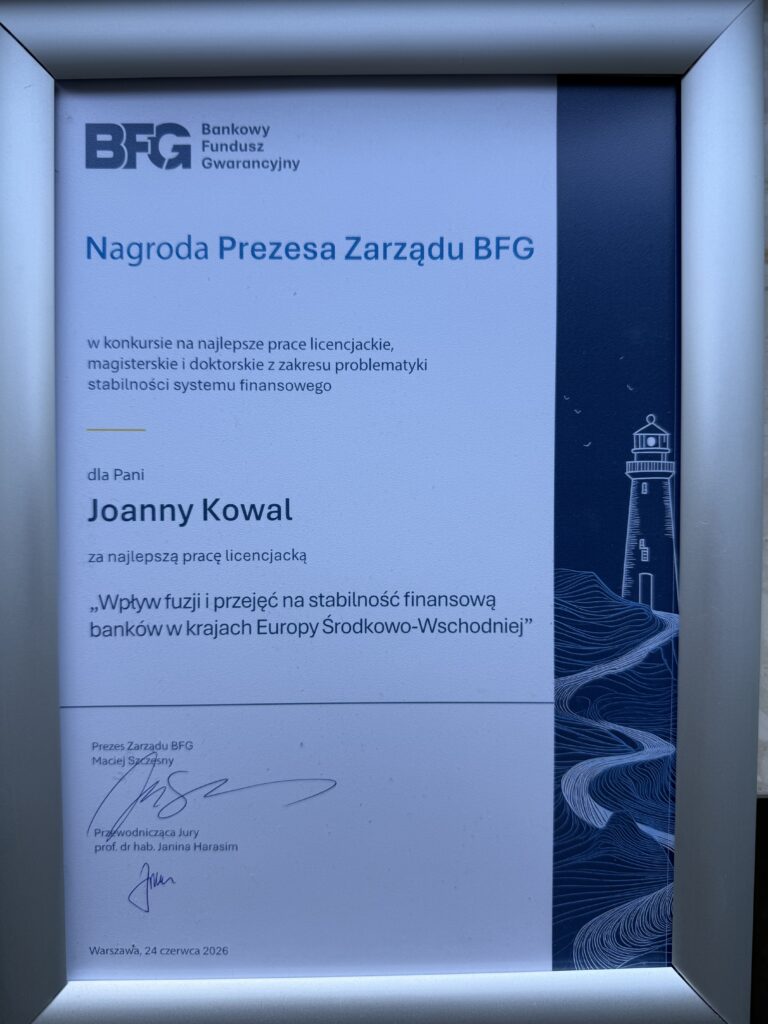 Oprawiony w srebrną ramę dyplom nagrody Bankowego Funduszu Gwarancyjnego leży na jasnej powierzchni. Dokument zawiera tekst, podpisy oraz ilustrację latarni morskiej w prawym górnym rogu. Zdjęcie przedstawia oficjalne wyróżnienie przyznane za osiągnięcia naukowe.