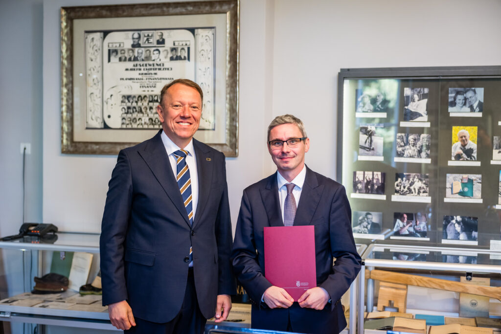 Dr hab. Mateusz Folwarski, prof. UEK, prezentuje dokument powołania na Kierownika Katedry Bankowości i Globalnego Systemu Finansowego, stojąc obok JM Rektora UEK dr. hab. Bernarda Ziębickiego, prof. UEK.