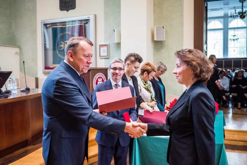 Uroczyste wręczenie wyróżnienia połączone z uściskiem dłoni podczas wydarzenia akademickiego.