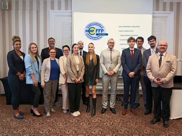 Grupa jedenastu osób w strojach biznesowych pozuje do wspólnego zdjęcia przed ekranem z logo i informacjami o wydarzeniu.