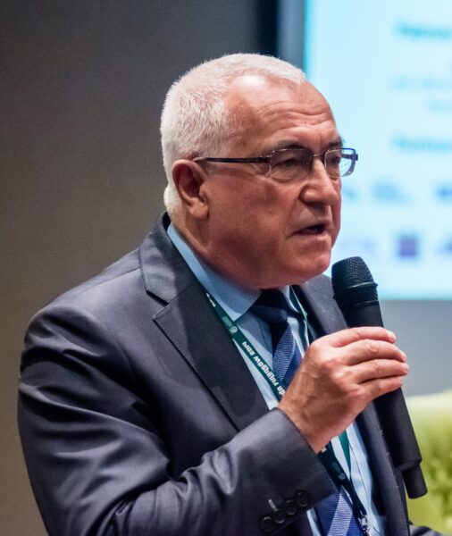 Krótko strzyżony mężczyzna w okularach, w dłoni trzyma mikrofon